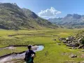 Un excursionista contempla un vasto valle de hecho, con un río serpenteante y montañas majestuosas bajo un cielo azul.