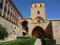 El **castillo de Alcañiz**, con su imponente torre y arcos, se alza bajo un cielo azul. Jardines cuidados y muros de piedra evocan su historia.