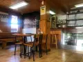 Mesas de madera y sillas listas para comer en Pontedeume. Barra con botellas y vasos, y un mural de la ciudad.