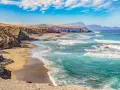 Paisaje de las playas de Fuerteventura con acantilados rocosos, arena dorada y el mar turquesa con olas rompiendo.