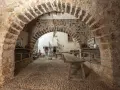 Interior de la torre de las arcas, con arcos de piedra, estanterías rústicas y un horno antiguo.
