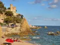 Castillo medieval sobre acantilados rocosos en sa caleta Lloret de Mar. Playa con gente y mar azul.