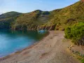 Tranquila cala Joncols plage con aguas turquesas, una persona paseando y barcas amarradas.
