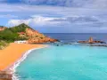 Hermosas calas cerca de Fornells, con arena dorada, aguas turquesas y casas blancas integradas en la costa rocosa.