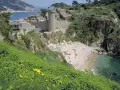 Vista de las calas de Tossa de Mar, con un castillo medieval y una playa con gente disfrutando del sol y el mar.
