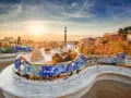 Bancos de mosaico coloridos en el Park Güell, un lugar imprescindible que ver en Barcelona, con la ciudad al amanecer.