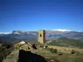 Antiguo muro de roda con torreón de piedra y ruinas, rodeado de montañas nevadas bajo un cielo azul intenso.