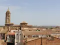 Vista aérea de un pueblo con tejados de teja, destacando una torre de iglesia con reloj. Hay mucho que ver en este pintoresco lugar.