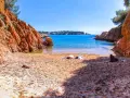 Arena dorada y aguas turquesas en la cala Maset. Dos personas toman el sol tranquilamente en la playa, rodeadas de imponentes rocas rojizas.