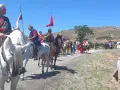 Un desfile ecuestre con trajes históricos, quizás recreando la gesta de el poyo del cid, avanza por un camino rural bajo un cielo azul.