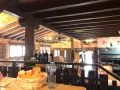Interior rústico de restaurantes en Llanes, con vigas de madera, ladrillo y una parrilla a la vista. Cesta de pan y botella de agua en primer plano.