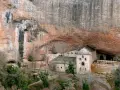 Monasterio de San Juan de la Peña, un impresionante conjunto arquitectónico excavado en la roca, con edificios de piedra y tejados a dos aguas bajo un gran saliente rocoso.