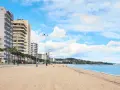 Amplia playa de arena dorada en la playa de Aro centro, con edificios altos a la izquierda y el mar azul a la derecha.