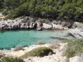 Es caló de la bella dona, una cala escondida con aguas turquesas y rocas escarpadas, donde algunos bañistas disfrutan del sol y el mar.