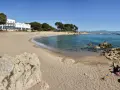Platja Cala de la Creu: arena dorada, aguas turquesas y un hotel blanco con vistas al mar. Familias disfrutan del sol y juegan en la arena.