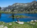 Persona sentada en roca contempla los lagos de Colomers en una ruta corta. Paisaje montañoso y azul intenso.