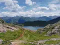 Sendero de montaña que conduce al sereno ibon de Estanes, rodeado de picos escarpados y un cielo azul con nubes algodonosas.