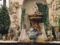 Fuente con estatuas y cabezas de piedra, evocando un antiguo castillo de gala.