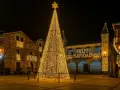 Árbol de Navidad gigante iluminado en una plaza, con edificios adornados y el mensaje "Feliz Navidad". Un lugar ideal que visitar en Navidad en España.
