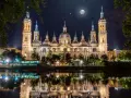 La majestuosa basílica del Pilar, iluminada bajo un cielo estrellado y la luna, se refleja en el río.