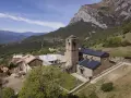 El monasterio de San Victorián, un conjunto de edificios de piedra con tejados oscuros, se alza majestuoso ante una imponente montaña rocosa.