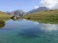 Un sereno ibón de espelunciecha refleja montañas y cielo azul.