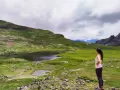 Mujer contempla los ibones del Valle de Tena, un paisaje de lagos y prados verdes bajo un cielo nublado.