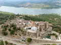 Vista aérea de Castellar de la Frontera, un pueblo blanco con un castillo, rodeado de vegetación y un embalse. Un lugar que evoca la paz de los hippies.