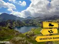 Paisaje de montaña con un lago azul, señalización de sendero y el letrero "SENDITUR BASIC", parte de la ruta de los 7 lagos Pirineos.