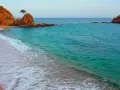 La platja mar menuda, con sus rocas anaranjadas y aguas turquesas, invita a soñar. Una ola rompe suavemente en la arena dorada.