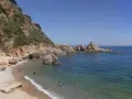 Les platges de Blanes ofereixen aigües cristal·lines i roques imponents sota un cel blau. Gent gaudeix del sol i del mar.