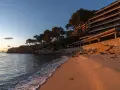 Atardecer dorado en la playa, con olas suaves lamiendo la arena. Al fondo, la silueta de la playa torre valentina se alza entre pinos.