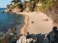 Una persona pasea por la cala belladona, con arena dorada y aguas cristalinas.