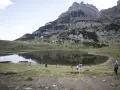 Gente paseando cerca de un lago en el valle de Tena, ideal para rutas de senderismo. Montañas escarpadas al fondo.