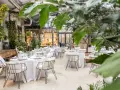 Mesas elegantemente puestas en un invernadero con vegetación exuberante. Un lugar ideal para saber donde comer en Madrid.
