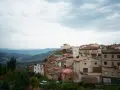 Pueblo español en ladera, con casas de tejados rojos y vistas a montañas. Se ven más de las matas verdes que rodean el asentamiento.