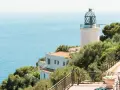 El faro de Sant Sebastià se alza sobre el mar azul, rodeado de vegetación exuberante.