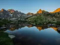 Reflejo dorado de montañas en un lago sereno del **parque natural Posets Maladeta** al amanecer.