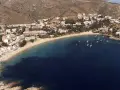 Vista aérea de la playa Almadrava en Roses, con edificios blancos y barcos anclados en aguas azules.