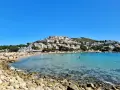 Vista de la platja de Montgó, con gente disfrutando del sol y el mar turquesa, y casas blancas escalonadas en la colina.
