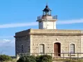 Faro de piedra con torre blanca y cúpula negra, vigilando el mar azul cerca del far port de la selva.