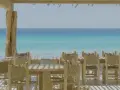 Mesas y sillas de madera rústica en la terraza de restaurantes en Formentera, con el mar turquesa de fondo.