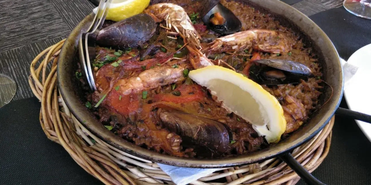 Paella marinera con gambas y mejillones, un plato típico de los restaurantes de Blanes, servida en una paellera sobre una cesta de mimbre.