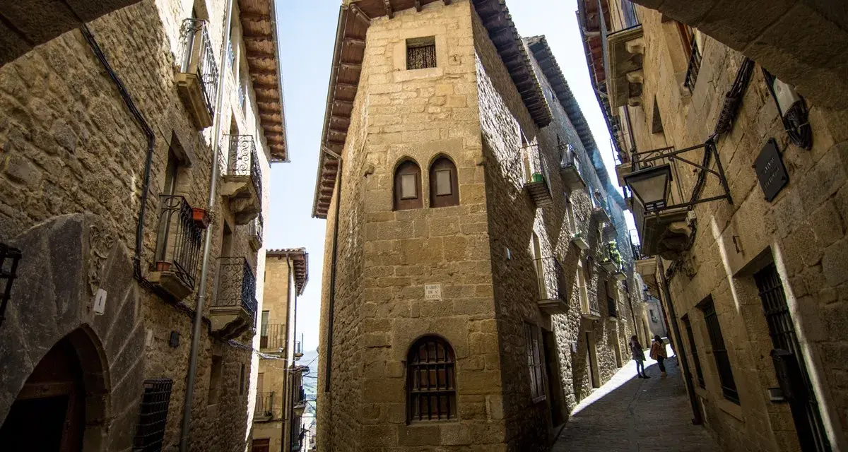 Calle empedrada con edificios de piedra, balcones de hierro y un arco. Un lugar que evoca la historia de los Reyes Católicos.