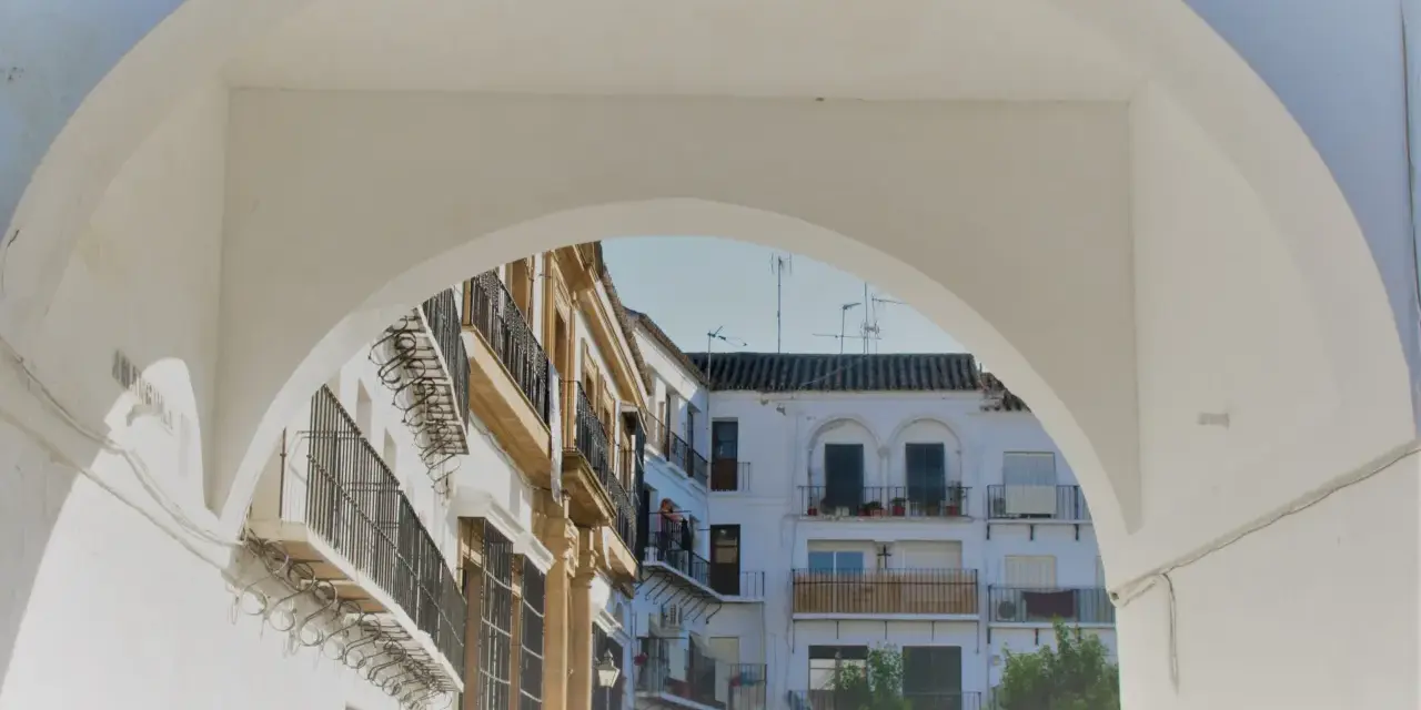 Un arco blanco enmarca edificios blancos y ocres con balcones de hierro forjado. Descubre qué ver en Marchena, un rincón andaluz lleno de encanto.