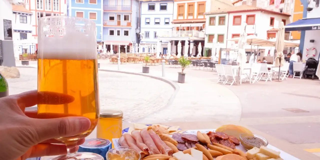 Disfrutando de una cerveza y una tabla de quesos y embutidos en Cudillero, con las coloridas casas de fondo.