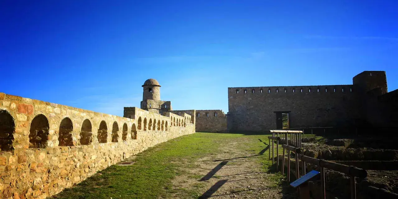Impresionante castillo de piedra con murallas, arcos y torreón. Un lugar histórico que ver en Benabarre, bajo un cielo azul intenso.