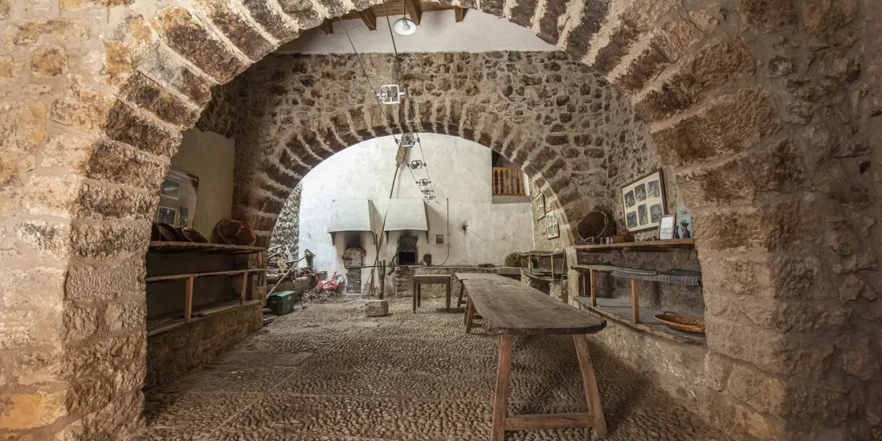 Interior de la torre de las arcas, con arcos de piedra, estanterías rústicas y un horno antiguo.