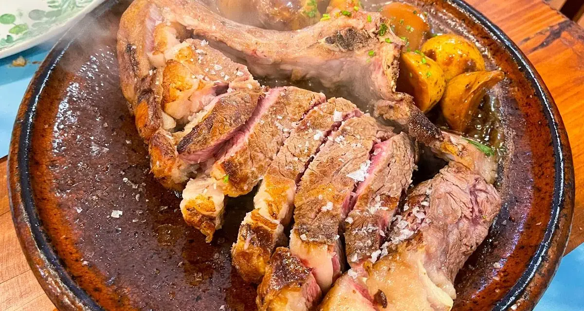 Un jugoso chuletón a la brasa, cortado y servido con patatas asadas, perfecto para comer en Tui.