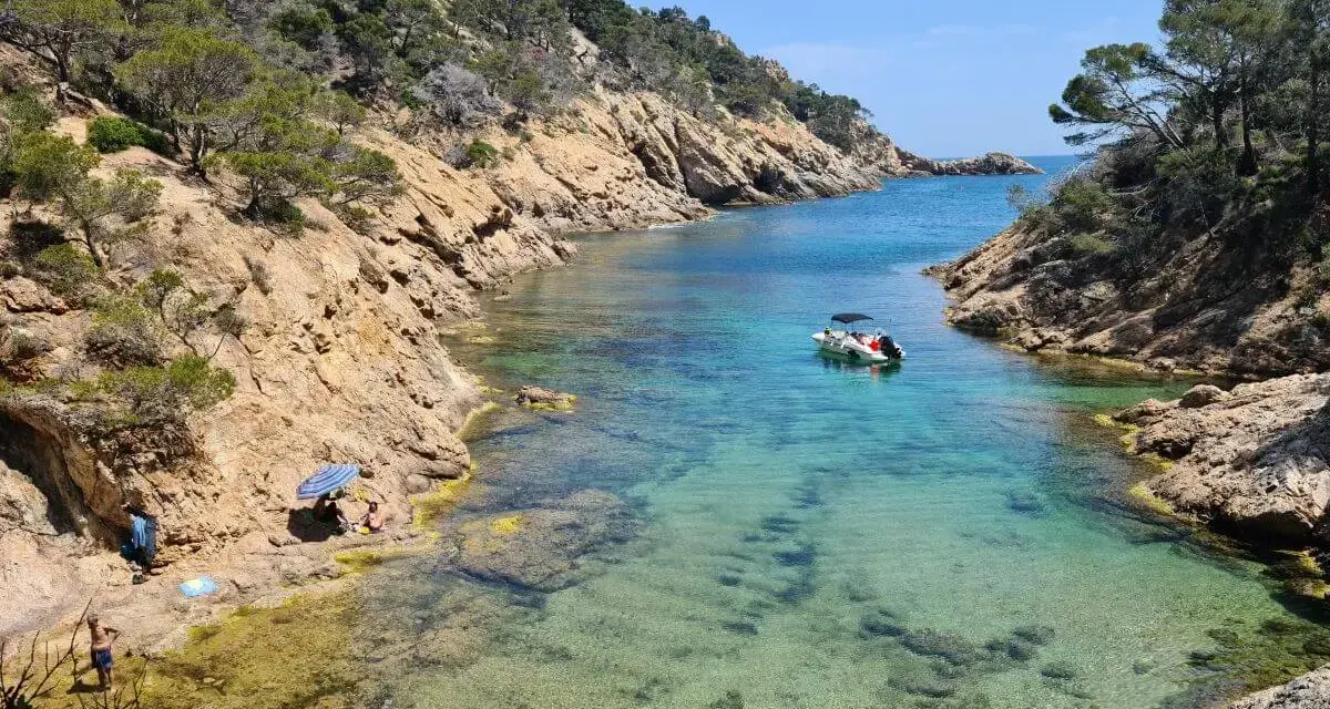 Una cala idílica en Tossa de Mar con aguas cristalinas, rocas escarpadas y un pequeño bote.